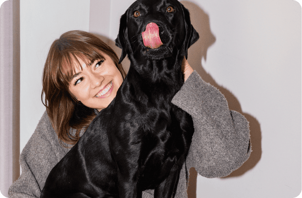 Frau umarmt lachend ihren Labrador, der die Zunge herausstreckt
